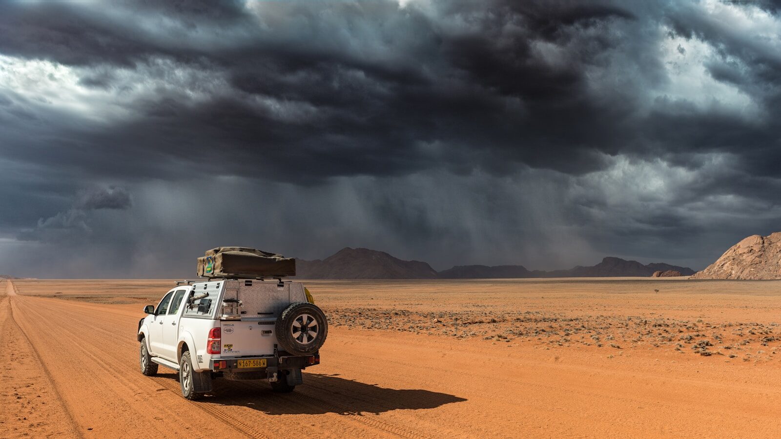 a car with a roof rack on the back of it driving down a dirt road